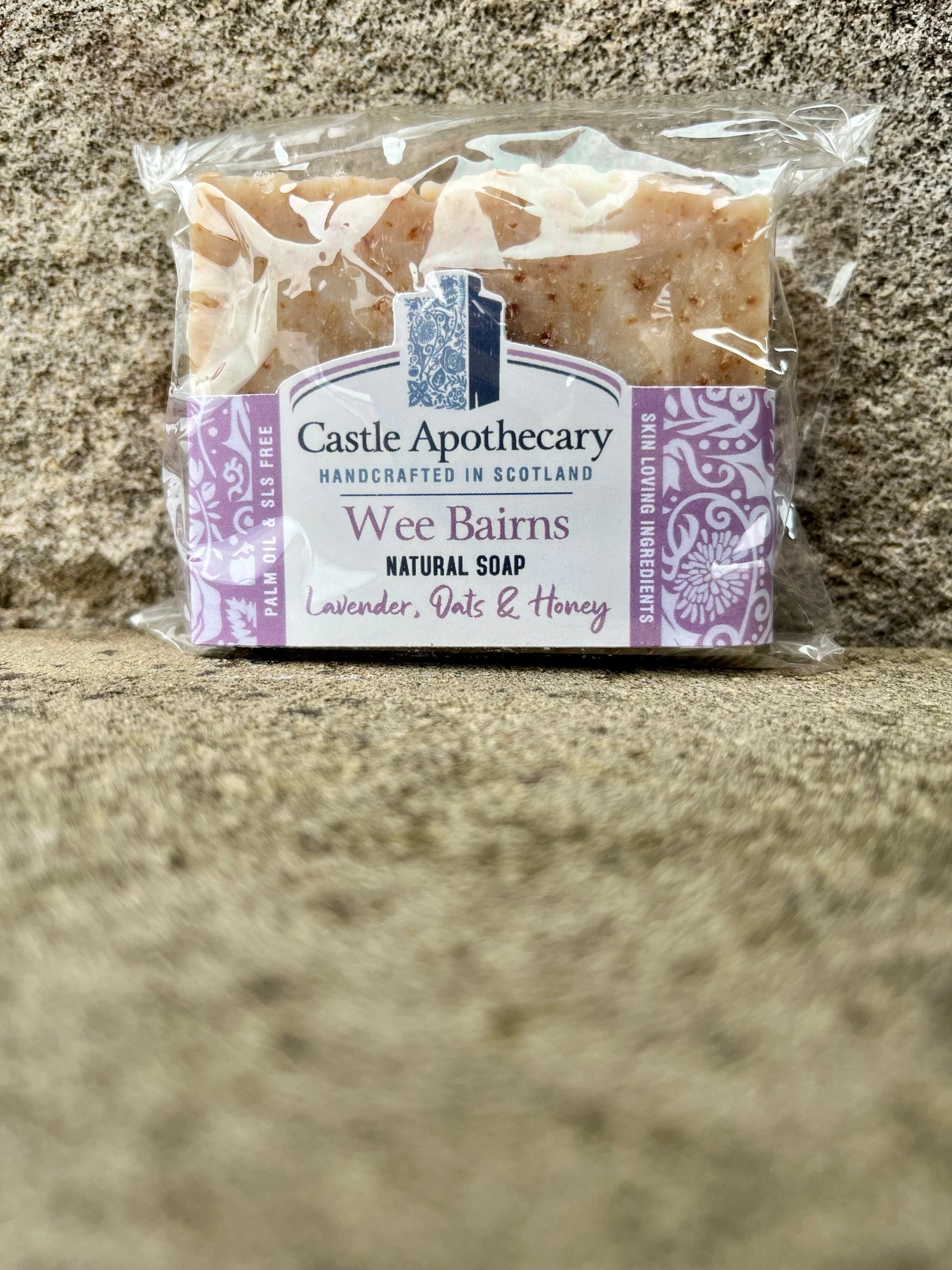 Wee Bairns Cold pressed Natural Soap Bar photographed against a castle stone background. Rectangular shaped hand crafted soap made with Scottish Oats, Honey and Gently scented with Lavender essential oil.  The rectangular bar can fit in a hand.